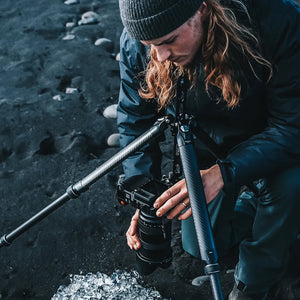 Fotograf mit Kamera auf einem Ulanzi Falcam TreeRoot Carbon-Stativ auf schwarzem Sand.